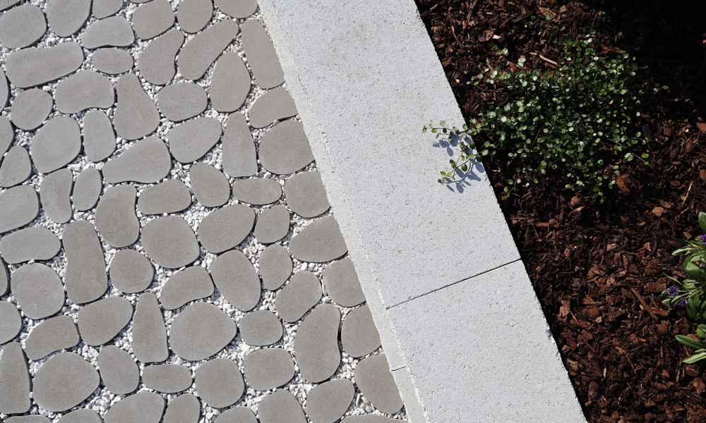 Kaviccsal feltöltött Dribbs gyeprács, Momento törtfehér falazóblokkal kombinálva magaságyáshoz. Esztétikus, növényekkel kombinált vízáteresztő burkolat a Friedl Steinwerke-től.