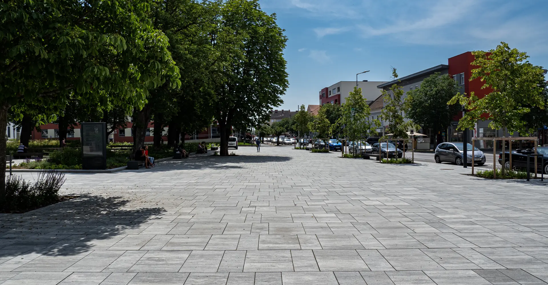 Széles tér fákkal az oberwarti városi kertben, az utca mentén; Magnum és Arret B25 VG4 térkő, gránitszürke árnyalt, Friedl Steinwerke.