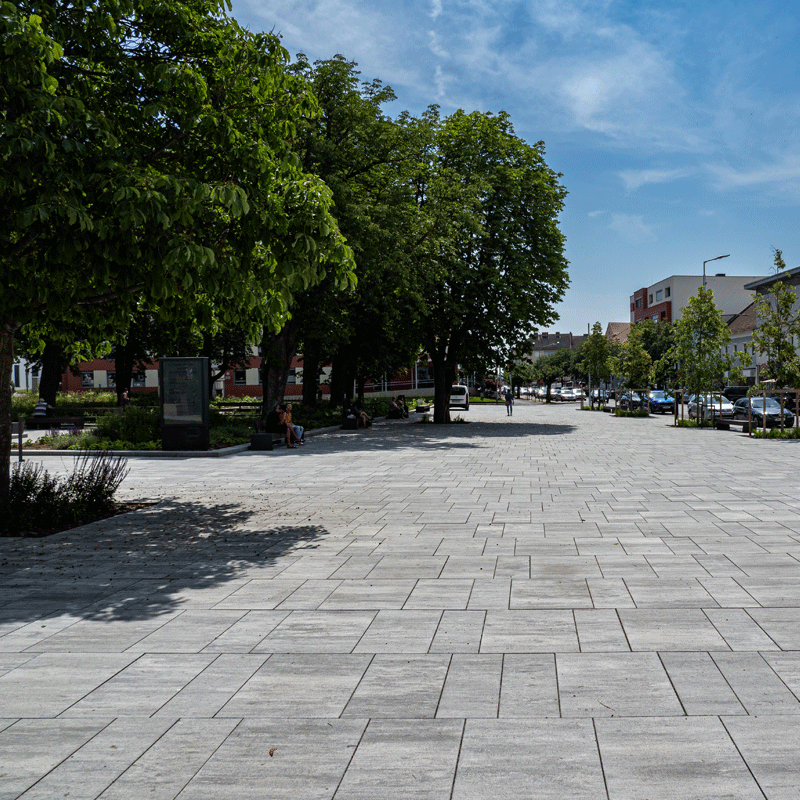 Stadtgarten Oberwart Magnum, gránitszürke árnyalt Tágas városi tér Oberwartban Magnum burkolattal, gránitszürke árnyalatban, fák és padok mentén, Friedl Steinwerke.