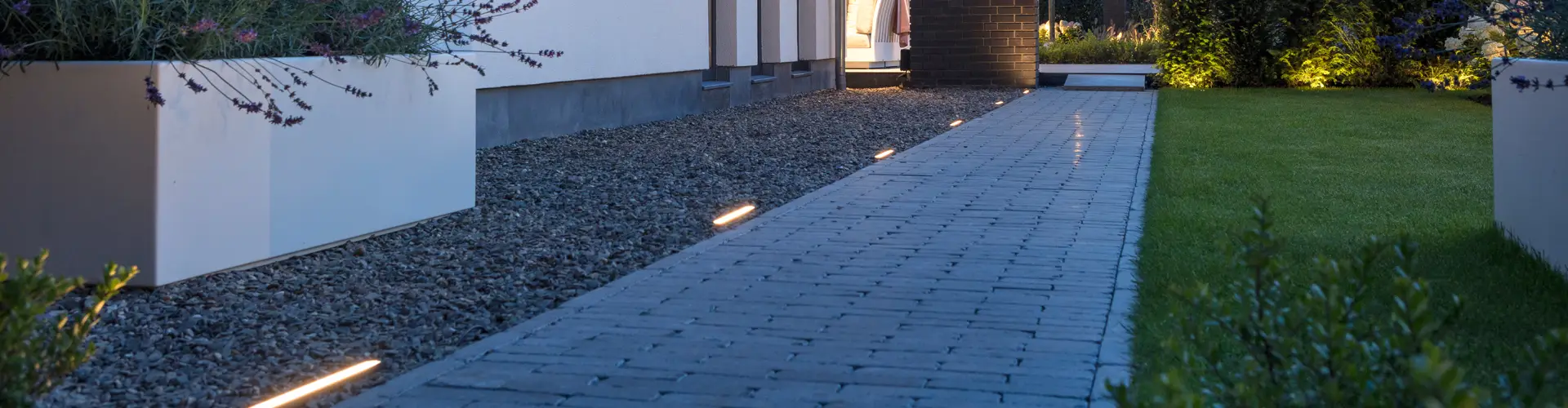 Stílusosan megvilágított járda Evo Ground 300 Dark lámpákkal az in-lite-tól, elérhető a Friedl Steinwerke kínálatában. A modern talajvilágítás elegáns hangulatot és biztonságos tájékozódást biztosít.