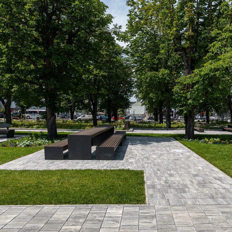 Stadtgarten Oberwart Arret B25 VG4 kombitérkő, gránitszürke árnyalt Oberwart városi park Arret B25 VG4 kombitérkővel, gránitszürke árnyalatban, padok és fák között, Friedl Steinwerke.